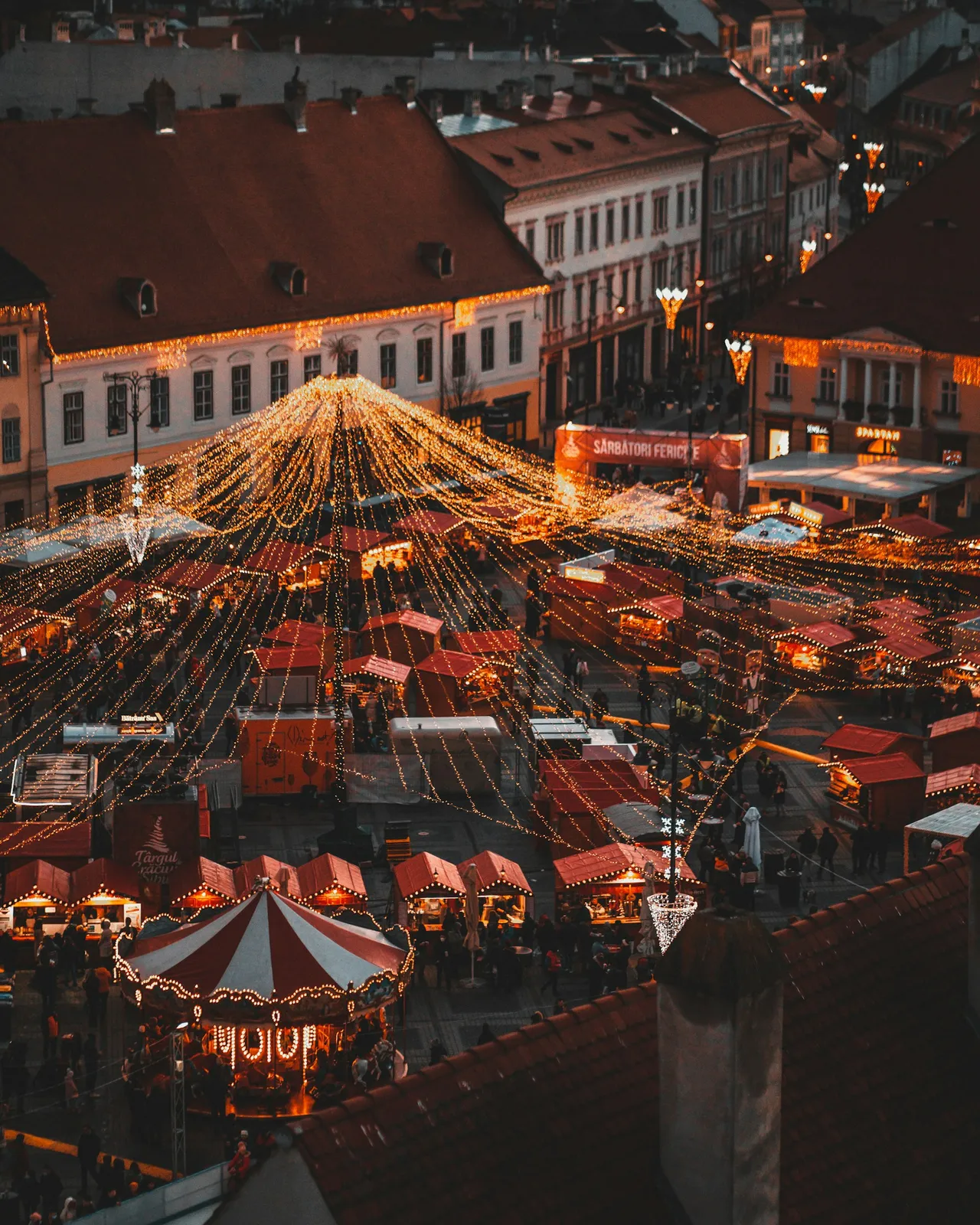 Aerial view of a holiday market at night, rows of stalls under string lights